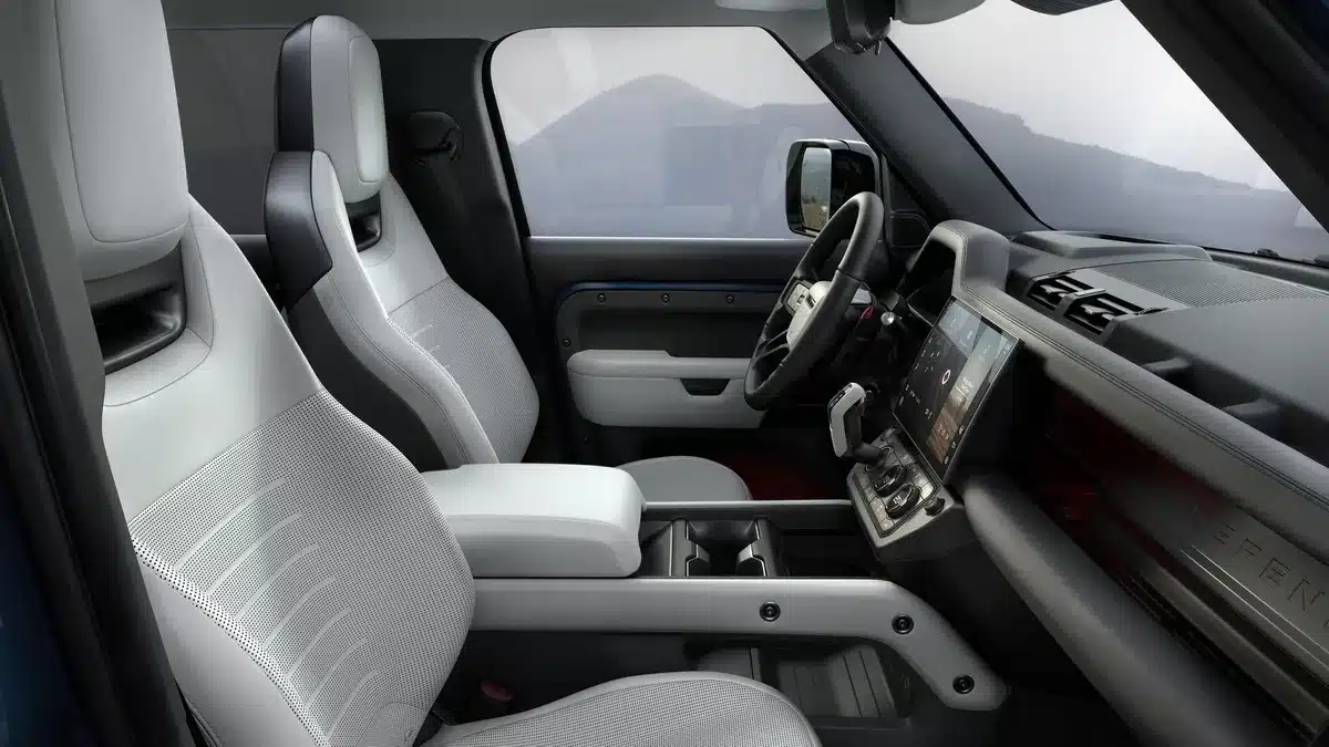 Manufacturer image of the 2026 Defender OCTA cabin showing light-colored front seats, steering wheel, dashboard and center touchscreen.